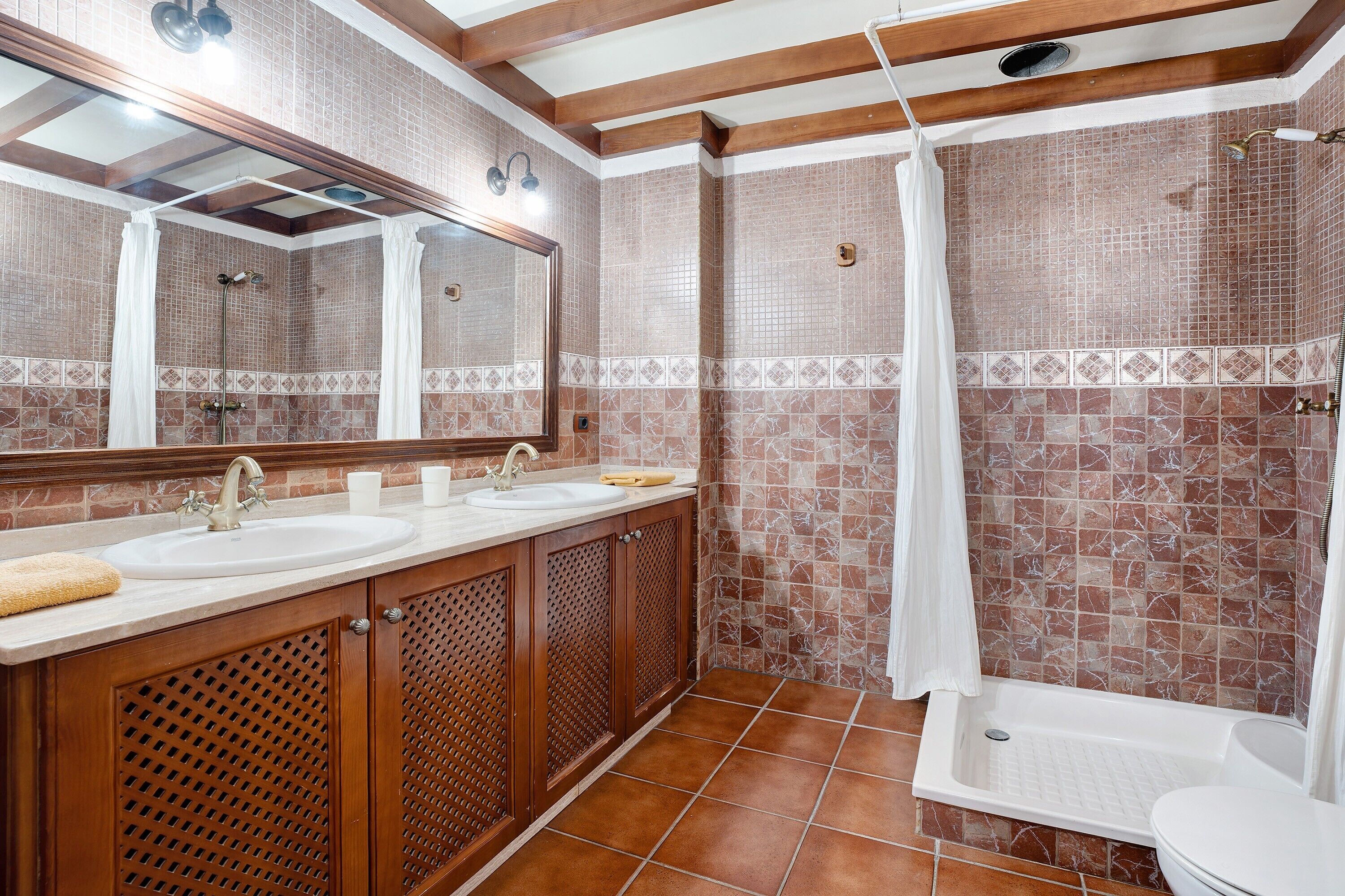 A bathroom with a double sink, a mirror, a shower, and tiled walls.