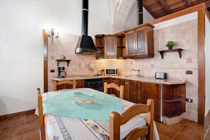 Eine kompakte Küche mit Holzschränken, einer Mikrowelle, einer Kaffeemaschine und einem Esstisch mit kariertem Tischläufer.