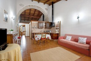 Un salon comprenant un canapé, une table à manger avec des chaises, un téléviseur et un coin cuisine avec une cuisinière et des placards.