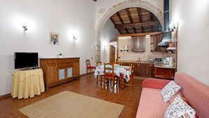 Un espace repas comprenant une table et des chaises, un canapé, un téléviseur et un coin cuisine avec des placards et une cuisinière.