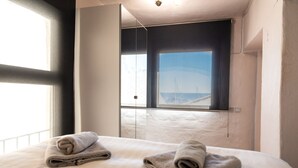 A hotel room with a bed, two towels, a window with a view, and a flat-screen TV mounted on the wall. - Chic Designer Apartment with Sea Views, Wi-Fi and Air Conditioning (Marbella)