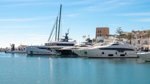 A marina with several yachts docked, a prominent building with a tower, and a clear blue sky. - Chic Designer Apartment with Sea Views, Wi-Fi and Air Conditioning (Marbella)