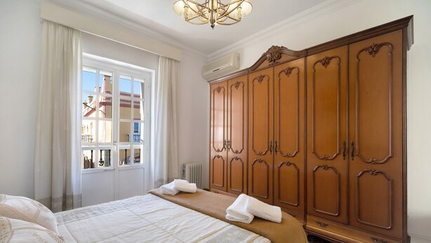 A hotel room with a large bed, a wardrobe, and a window with curtains. - Apartment 'Casa Macarena' with Private Terrace and Balcony (Chiclana de la Frontera)