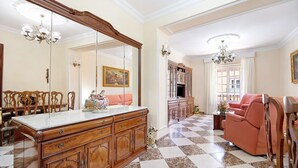 A spacious room with a large wooden cabinet, a sofa, and a dining area with chairs. - Apartment 'Casa Macarena' with Private Terrace and Balcony (Chiclana de la Frontera)