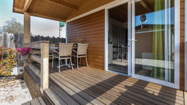 Une terrasse en bois dotée d’un espace salon couvert, de portes-fenêtres coulissantes donnant sur l’intérieur et d’une clôture en bois.
