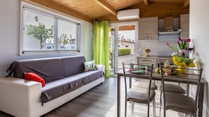 Un salon moderne comprenant un canapé, une table à manger avec des chaises, un coin cuisine et une fenêtre donnant sur des arbres et des immeubles.