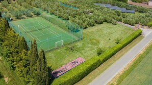 En vy från ovan av ett sportkomplex med en tennisbana, solpaneler och omgivande grönska.