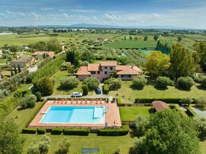 Una casa grande con piscina, rodeada de jardines cuidados y vistas a montañas distantes.