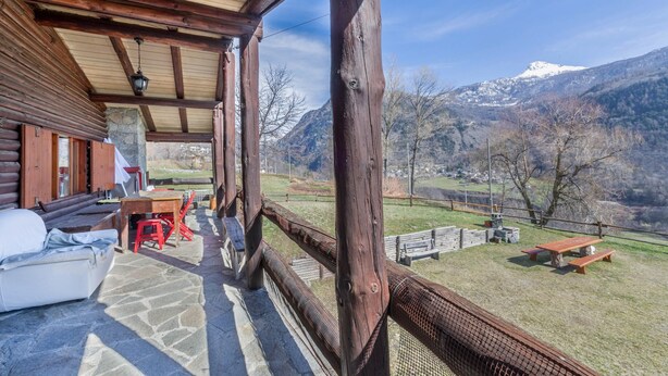Une cabane en bois avec un plancher en pierre, une véranda et une vue sur des montagnes enneigées.