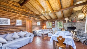 L’intérieur d’une cabane en rondins, avec un canapé, une table à manger, une cheminée et des poutres en bois.