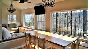 A cozy living room with a large window, a dining table, and a ceiling fan.