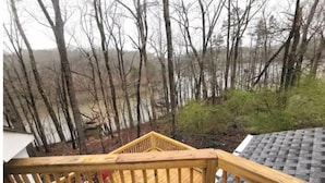 A wooden deck with a railing overlooking a forested area and a body of water.