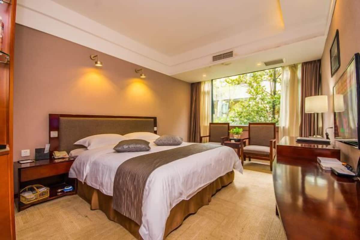 Une chambre d’hôtel avec un grand lit, des tables de chevet, un bureau et une vue sur la verdure.
