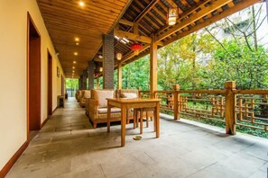 A covered corridor with wicker furniture and a wooden railing overlooking a garden. - Mount Forest Hotel (Emeishan City)