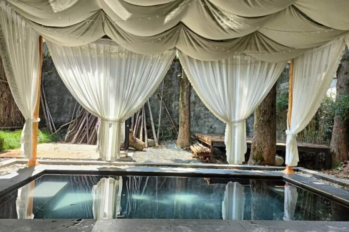 Une piscine à l’eau claire, entourée de tentures blanches et de structures en bois.