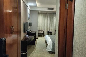 Een hotelkamer met een bed, een bureau met stoel, een televisie en een raam met gordijnen.