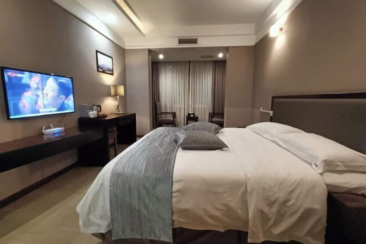 Une chambre d’hôtel avec un lit, un bureau avec une télévision, une chaise et une fenêtre avec des rideaux.