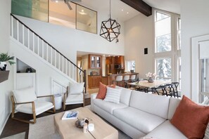 A spacious living area with a white sofa, wooden chairs, a coffee table, and a staircase leading to an upper level. - Step onto Ski Hill 3-Bedroom: Hot tub, Parking, AC (Whistler)