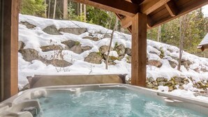 Un jacuzzi en un pabellón de madera con montañas nevadas al fondo.
