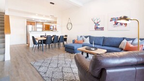 Una sala de estar moderna con un sofá azul, un sillón de cuero y una zona de comedor con una mesa y sillas de madera.