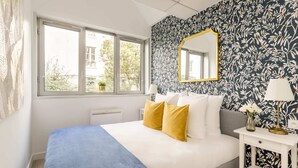 Une chambre à coucher avec un lit, une table de chevet avec une lampe, une fenêtre et un miroir au mur.