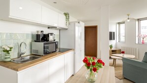 Une cuisine moderne avec des meubles blancs, un évier en acier inoxydable et un four à micro-ondes. On y trouve également un coin repas avec une table et un canapé bleu.