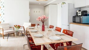 A modern dining area with a long table set for six, surrounded by orange chairs. A vase with pink flowers is on the table. - Family Suite - Tour Eiffel - Viala II (Paris)