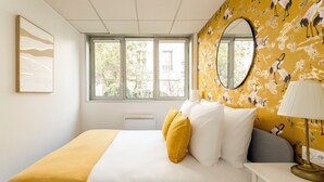 A bedroom with a bed, a bedside table, a lamp, a window, and a wall with a mural. - Family Suite - Tour Eiffel - Viala II (Paris)