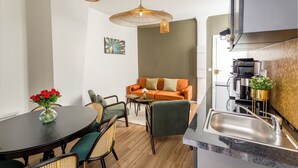 A modern kitchen with a stainless steel sink, a dining area with a round table and chairs, and a sofa with cushions. - Family Suite - Opera - Caumartin II (Paris)