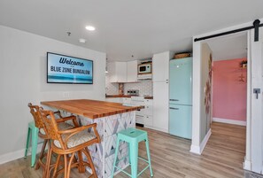 Una cocina con una isla de madera, armarios blancos, un refrigerador azul turquesa y un cartel que dice 'Welcome to the BLUE ZONE BUNGALOW'.