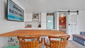 A modern kitchen with a wooden table and wicker chairs, a microwave, and a refrigerator. - Blue Zone Bungalow! 150 yards to the beach & close to cafes! (Wrightsville Beach)