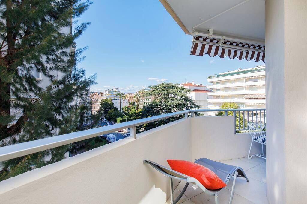 Un balcon avec une balustrade en métal, une chaise avec un coussin rouge et une vue sur des immeubles et des arbres.