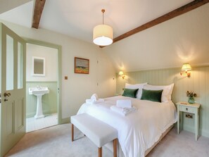 Une chambre à coucher comprenant un lit, un banc, une table de chevet, une lampe et une porte donnant sur une salle de bain.