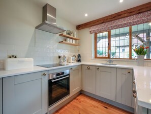 A modern kitchen with white cabinets, a stainless steel range hood, a built-in oven, and a window with a view of the outside. - 1 bedroom accommodation in Pulborough (Pulborough)