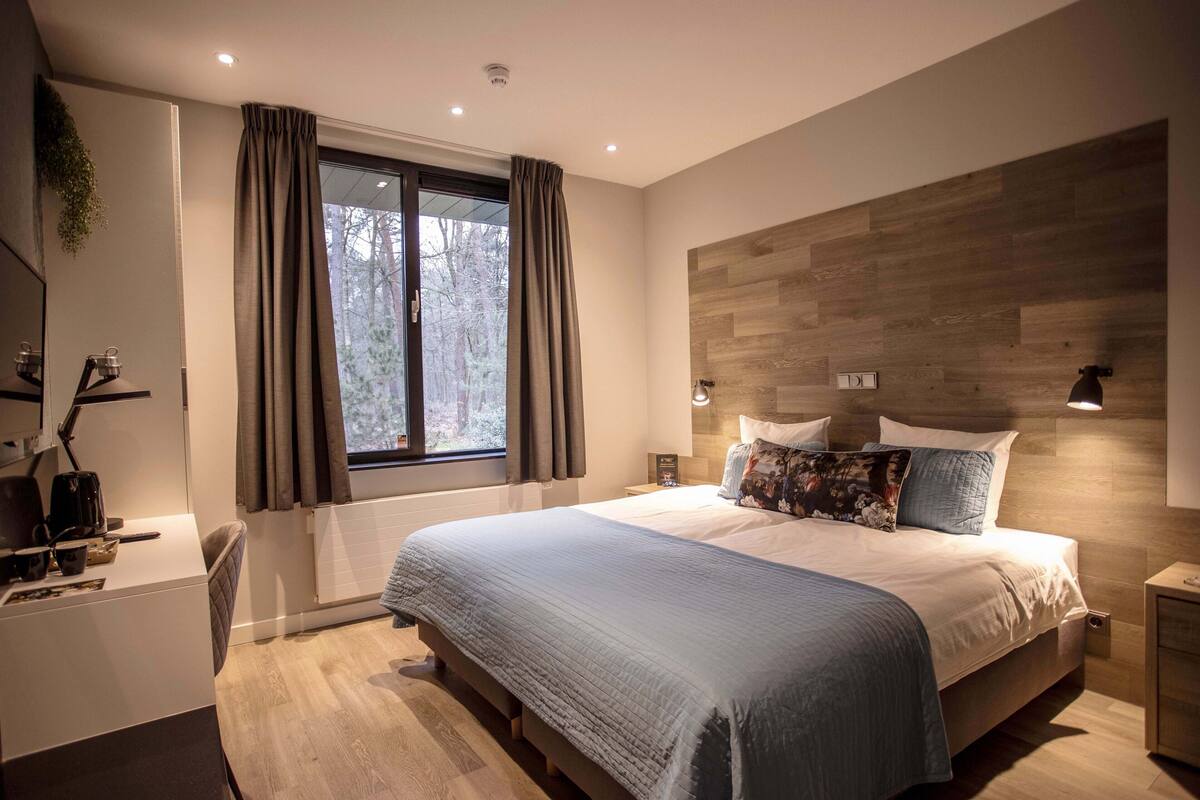 Een moderne slaapkamer met een groot bed, een bureau en een raam met gordijnen.