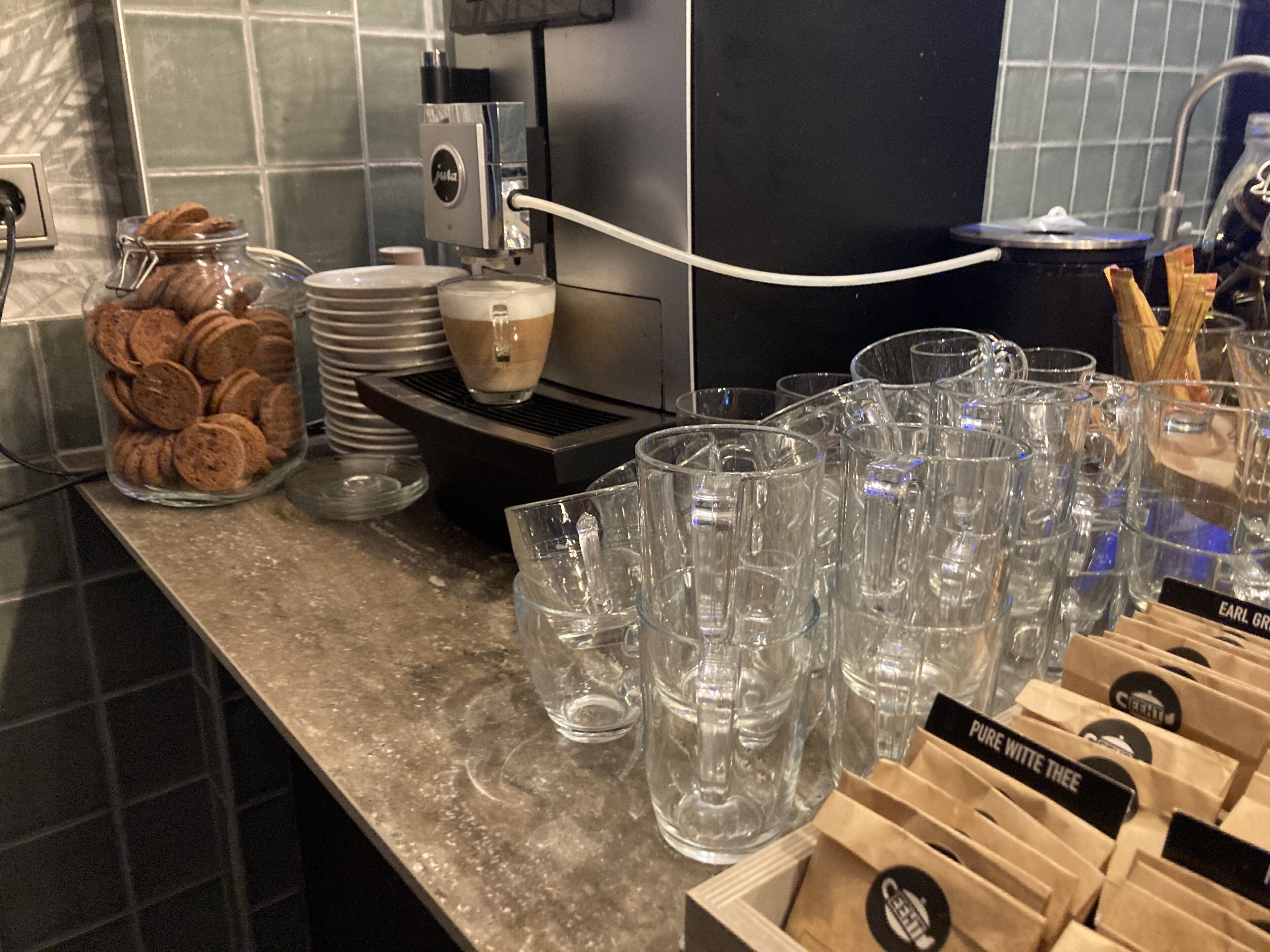 Una encimera de cocina con una cafetera, un tarro de galletas y varios vasos.