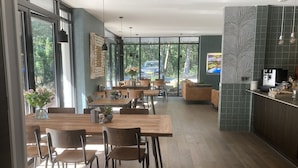 A modern dining area with wooden tables and chairs, large windows, and a kitchen area with a coffee machine. - Boutique Hotel Bed & Bos (Best)