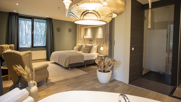 A modern bedroom with a large bed, a sitting area, and a bathroom with a shower. - Boutique Hotel Bed & Bos (Best)
