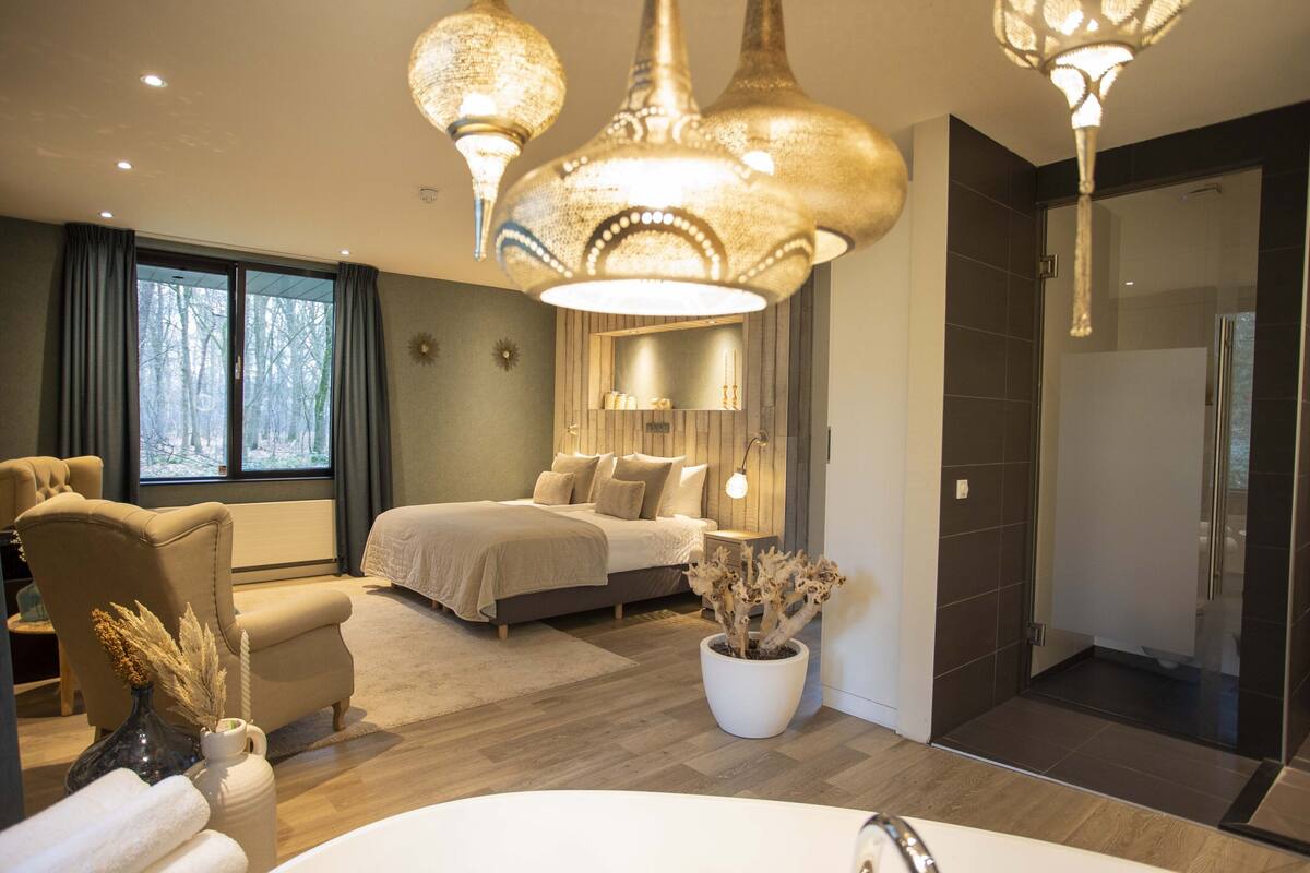 Een moderne slaapkamer met een groot bed, een zithoek en een badkamer met douche.