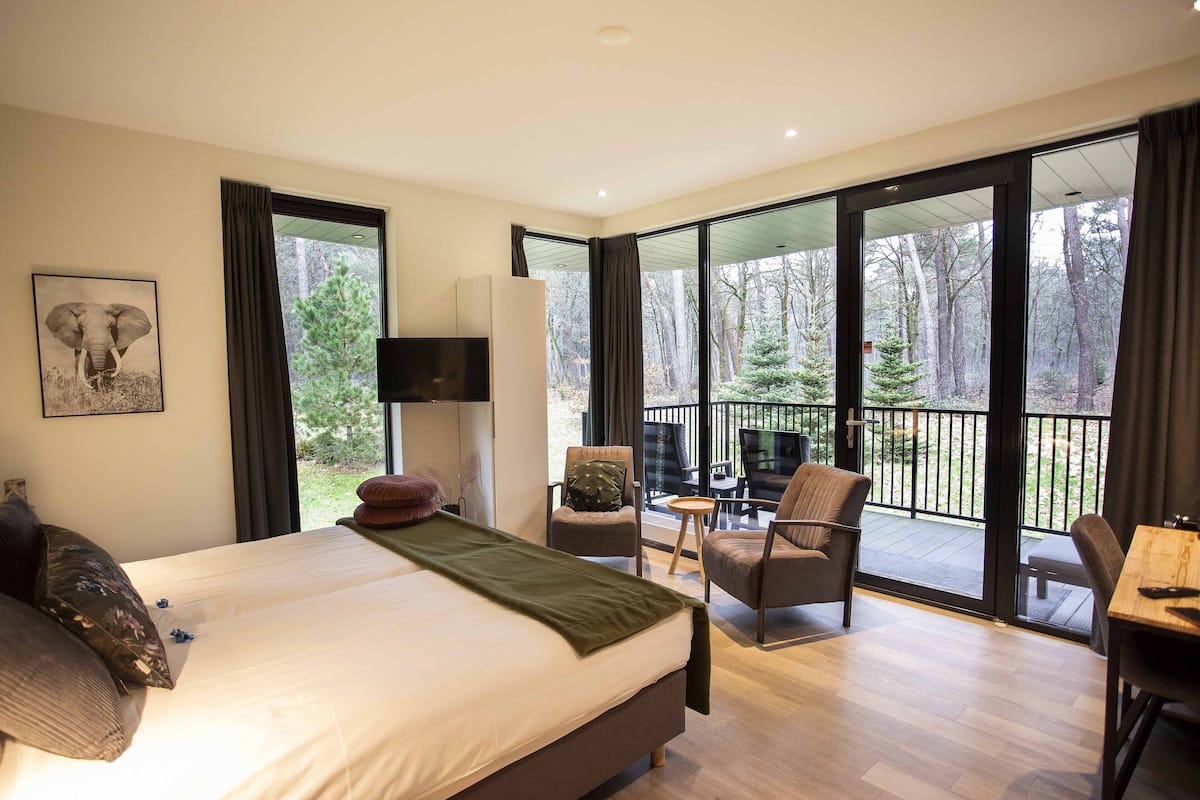 Een moderne slaapkamer met een groot bed, een televisie, en een balkon met stoelen en een tafel.