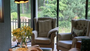 A cozy living room with large windows, a comfortable sofa, a wooden coffee table, and a chair with a cushion. - Boutique Hotel Bed & Bos (Best)