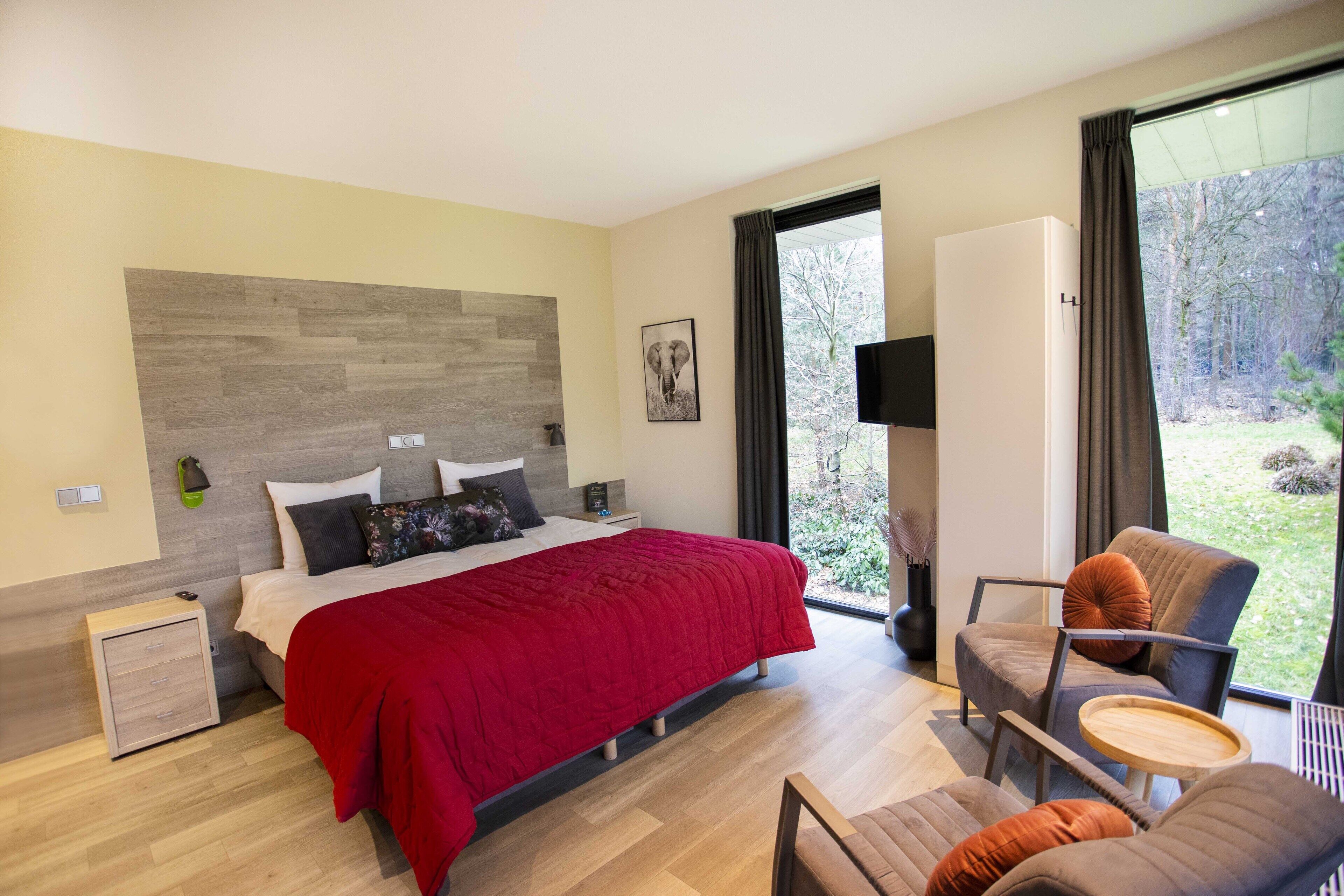 A modern bedroom with a large bed, a chair, a small table, and a TV.