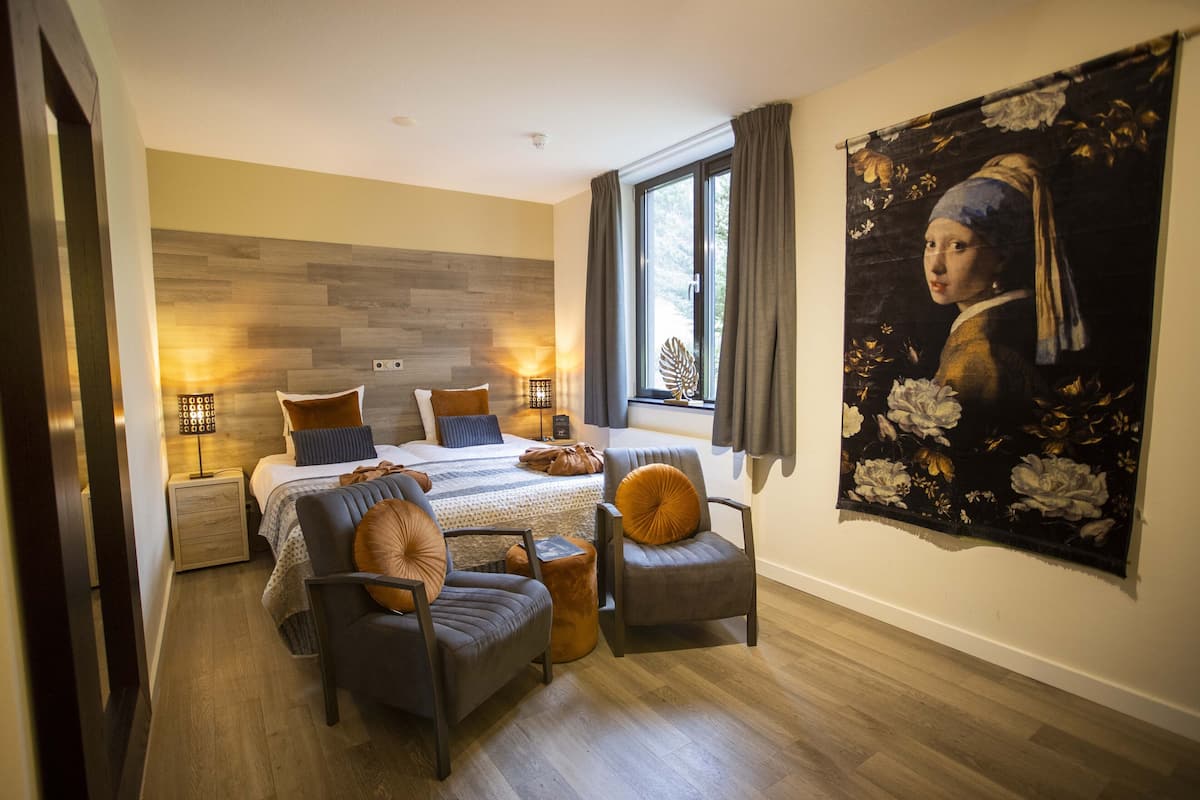 Een moderne slaapkamer met een groot bed, twee nachtkastjes, een stoel en een groot schilderij aan de muur.
