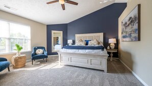 Une chambre à coucher avec un lit, un ventilateur de plafond, une fenêtre et une chaise.