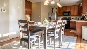 Un coin repas avec une table et des chaises en bois, un lustre et une cuisine en arrière-plan.