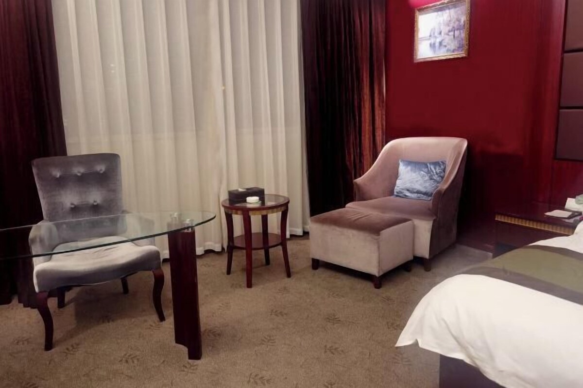 A hotel room with a glass table, two armchairs, a bed, and a small round table with a candle.