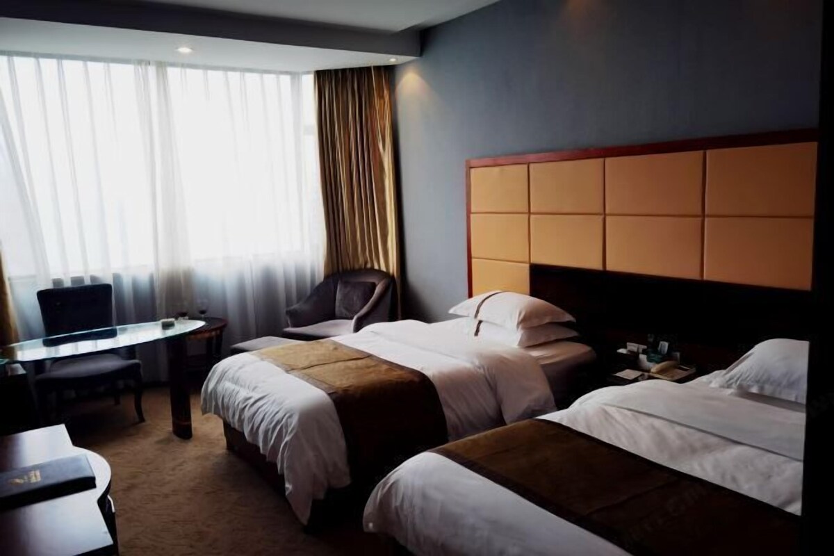 A hotel room with two beds, a desk, a chair, and a large window with curtains.