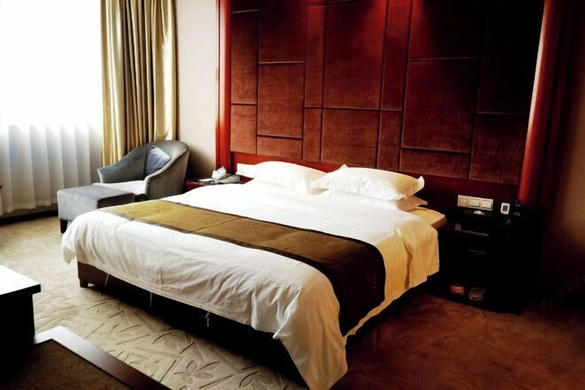 A hotel room with a large bed, a chair, a bedside table, and a red headboard.