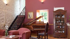 Una habitación con un piano de cola, una estantería llena de licores, una escalera y un suelo cubierto de alfombra roja.