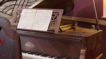 A grand piano with sheet music on top, placed in a room with a stone floor and a wrought iron railing.